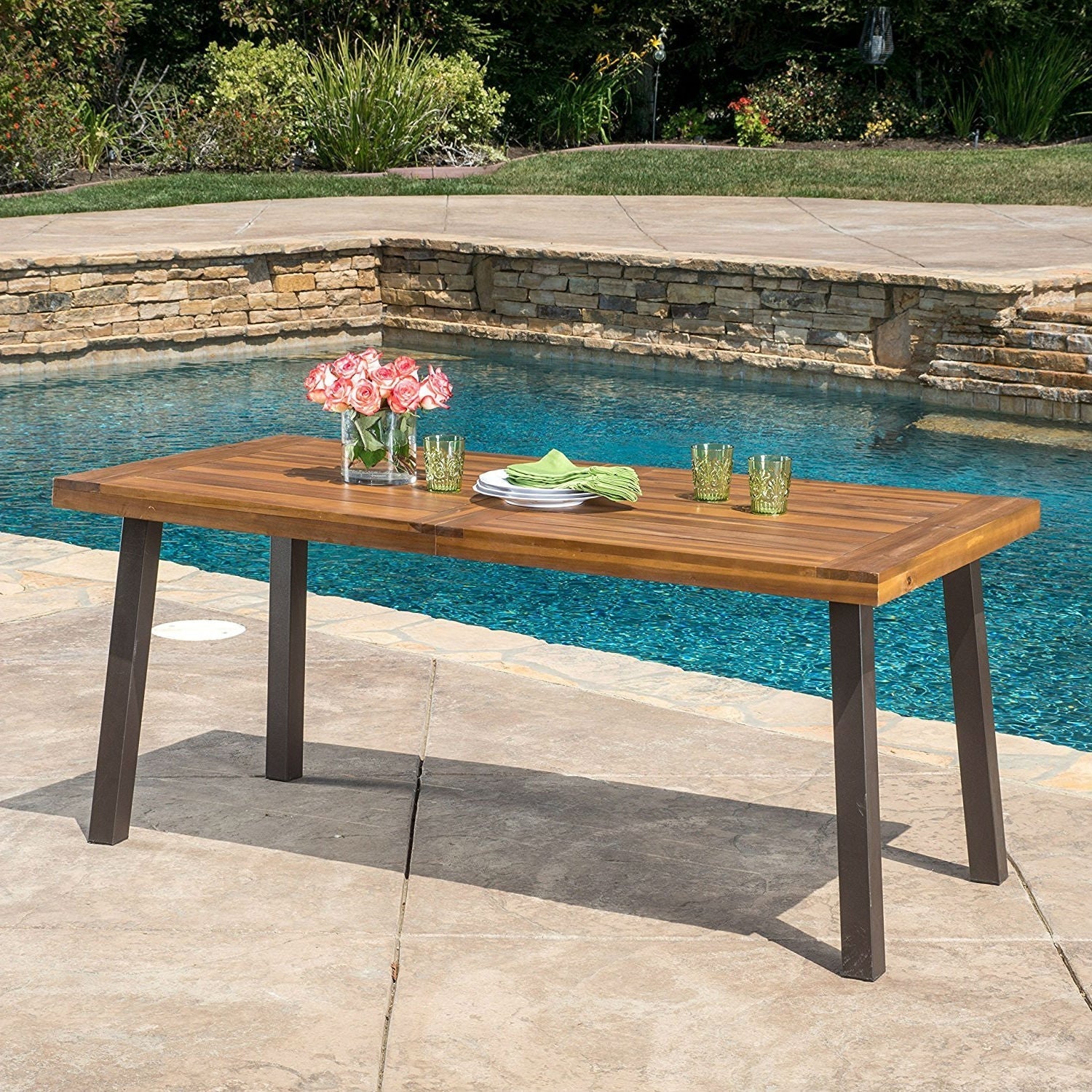 Outdoor dining table with flowers and glasses by a pool, perfect for home and garden decor.